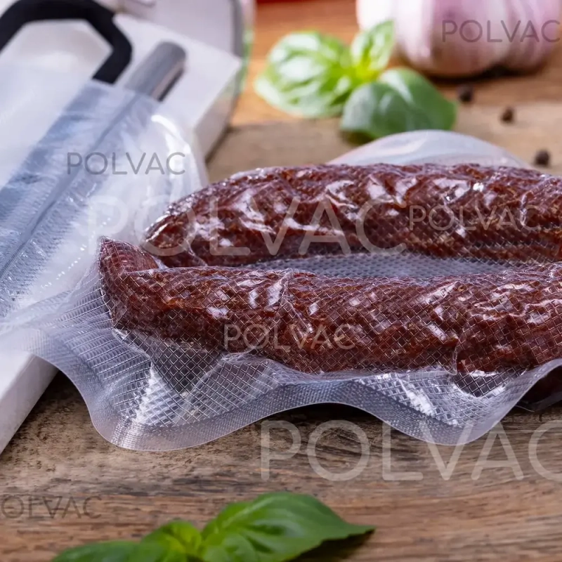 Kiełbasa  zapakowana w moletowany rękaw próżniowy marki Polvac, leżąca na drewnianym blacie obok domowej zgrzewarki próżniowej